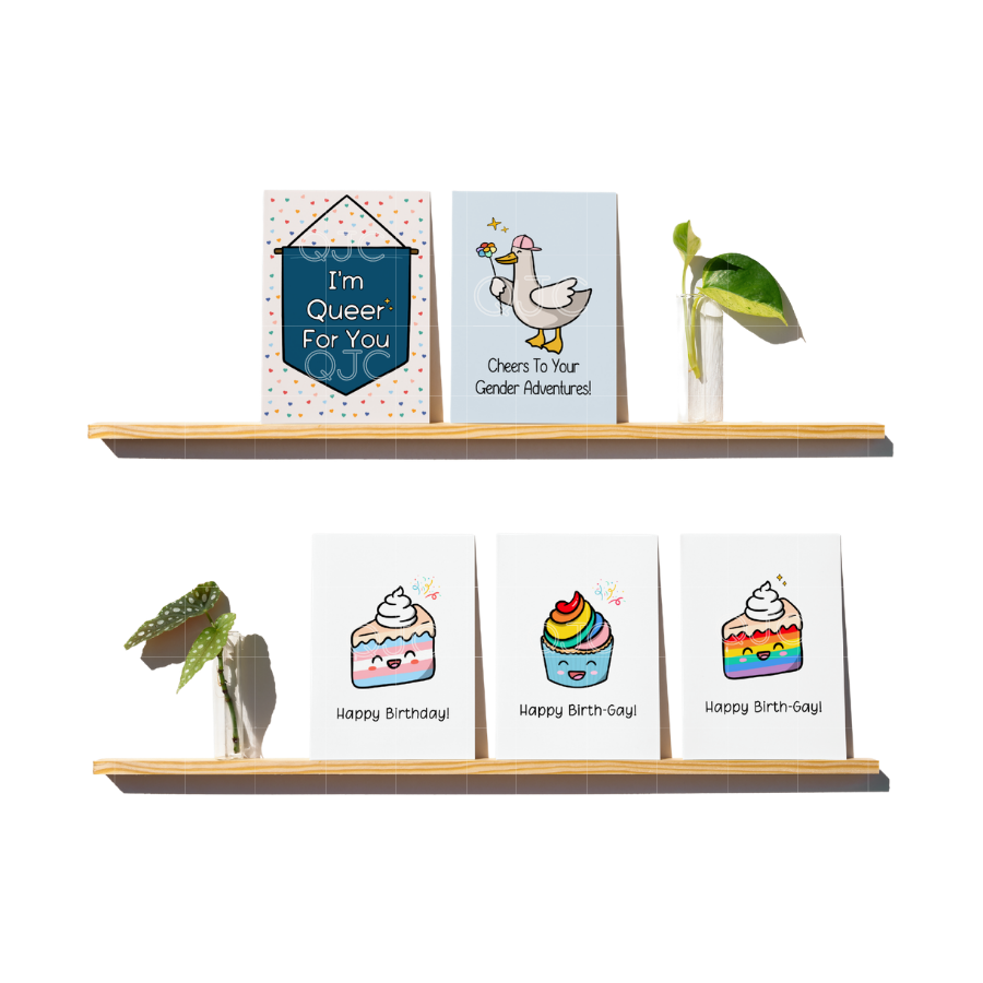 Two shelves holding plants and five cards, one that says I'm Queer For You, One that has a Duck and says Cheers to your gender adventures, and one with a trans piece of cake, a rainbow cupcake and rainbow slice of cake